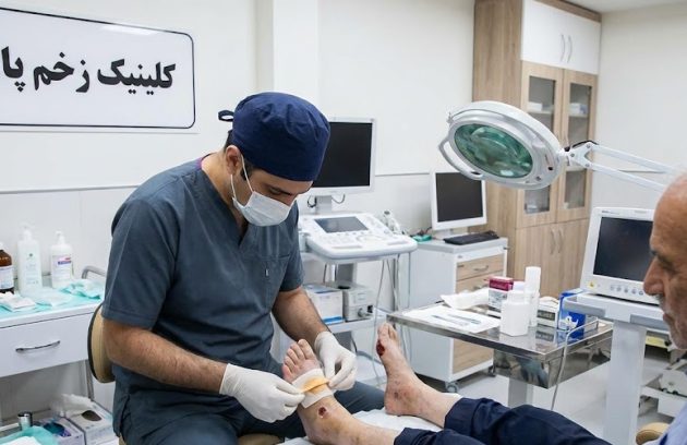 پزشک متخصص در حال انجام مراحل مراقبتی و پانسمان تخصصی بیمار سالمند به عنوان بخشی از پروسه درمان قطعی زخم پای دیابتی در کلینیک پاشنه.