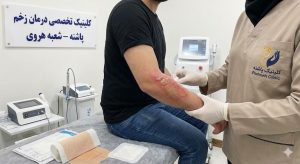 متخصص کلینیک پاشنه در حال معاینه و درمان تخصصی زخم سوختگی روی دست بیمار در شعبه هروی.
