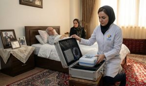 کارشناس زخم کلینیک پاشنه پس از رسیدن به منزل بیمار در تهران، در حال باز کردن کیف تجهیزات تخصصی بر بالین بیمار سالمند جهت شروع درمان زخم بستر عمیق.