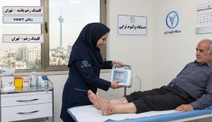 پرستار در حال انجام وکیوم تراپی زخم پای بیمار دیابتی در کلینیک تخصصی در تهران با نمای برج میلاد.