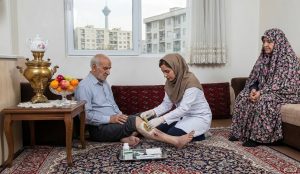 پرستار در حال انجام لارو درمانی در منزل یک خانواده ایرانی در تهران با حضور مادربزرگ و منظره برج میلاد.
