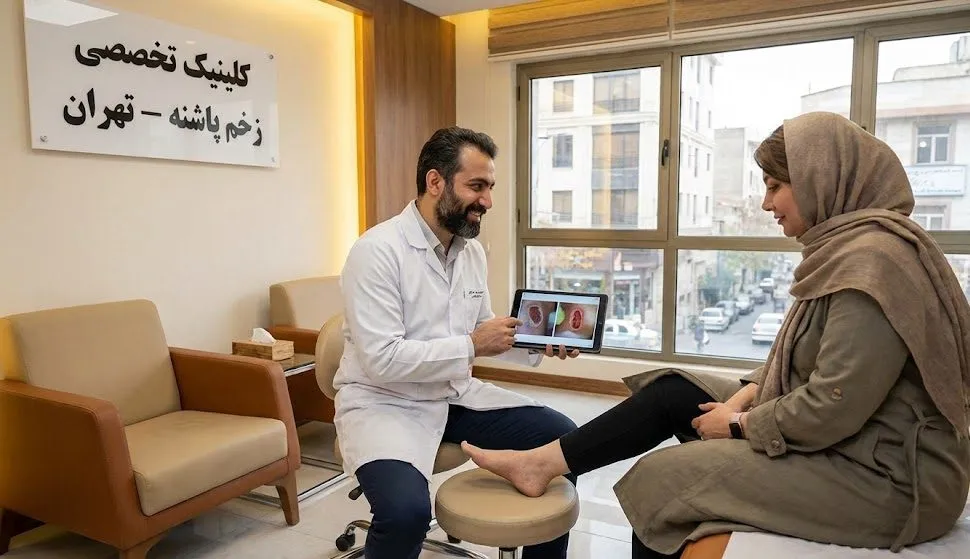 پزشک متخصص در حال مشاوره با بیمار و استفاده از ماکت پا و تبلت برای توضیح مراحل جراحی سرپایی زخم در تهران در محیط کلینیک.