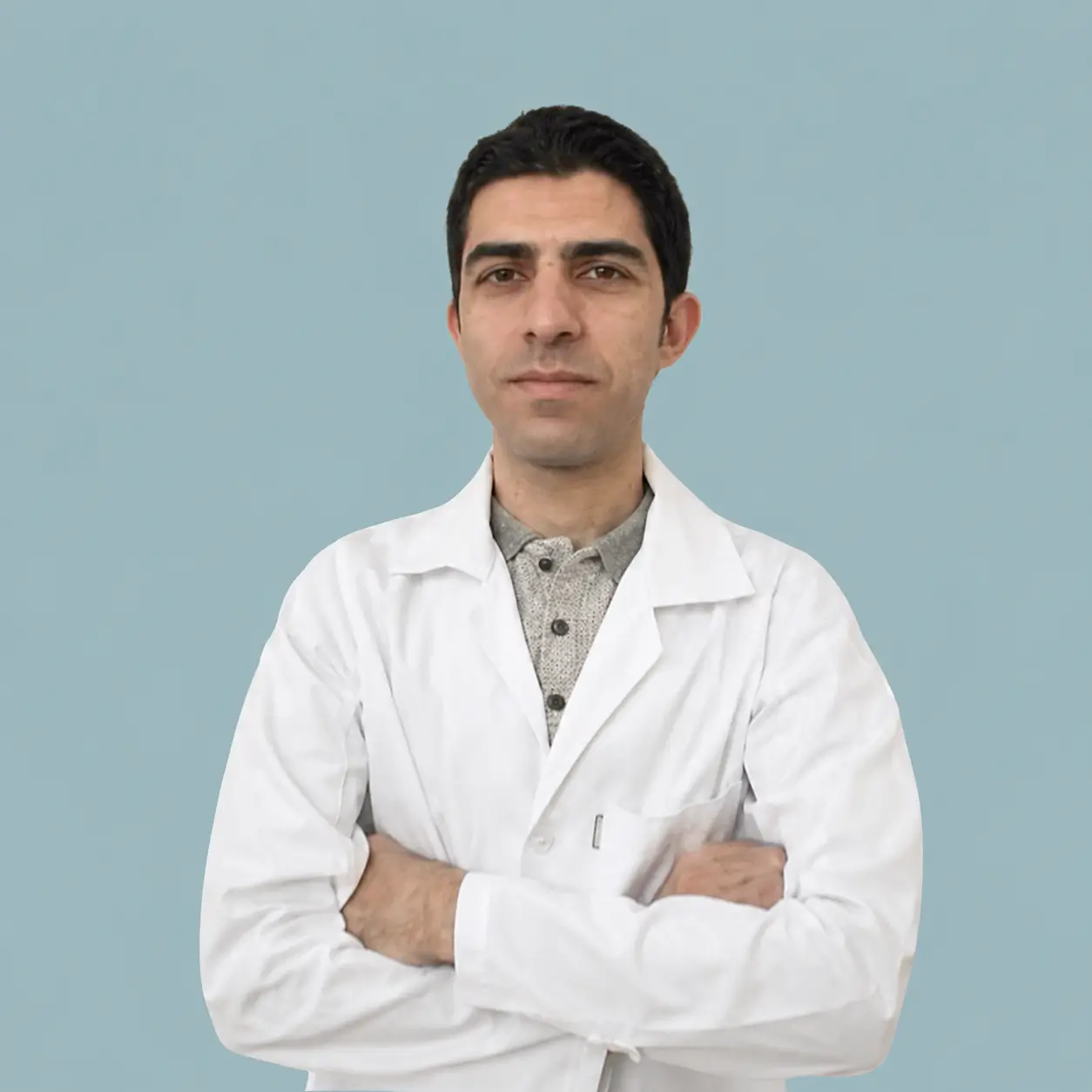 پرتره رسمی دکتر سید حسین ملک پور، دکتری علوم آزمایشگاهی و متخصص تشخیص عفونت با کت آزمایشگاهی سفید، دست‌های ضربدری و گردنبند نقره، در برابر پس‌زمینه آبی-خاکستری.